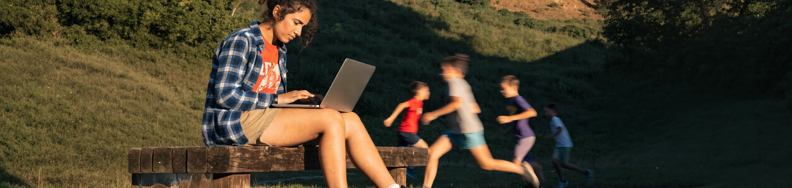Monitora trabajando con el portátil mientras un grupo de niños corre en el campo
